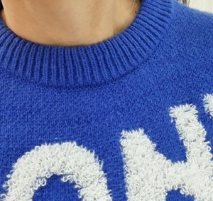 Close-up of blue knit sweater with round neck and white chenille letter embroidery detail