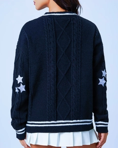 Detail of navy knit sweater showing chunky cable pattern and white star embroidery on sleeve
