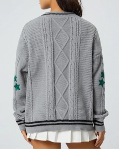 Close-up of cable knit patterns and green star patch embroidery on the grey sweater sleeve