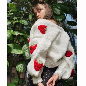 Detail of chunky white knit cardigan featuring 3D strawberry appliques and knit texture