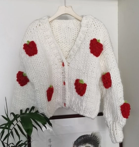 Close-up of white chunky knit cardigan featuring 3D strawberry motifs and red buttons