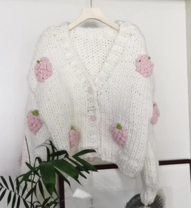 Detail of chunky knit white V-neck cardigan featuring 3D handmade strawberry crochet accents