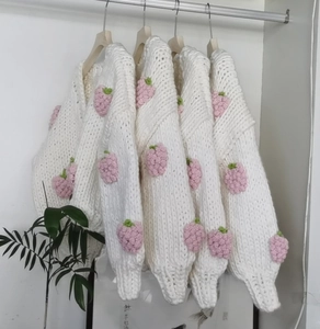 Close-up of hand-crocheted chunky knit cardigan with 3D pink strawberry patterns