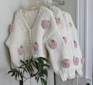 Close-up of chunky knit white cardigan featuring handcrafted 3D strawberry appliques