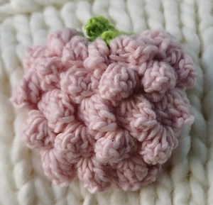 Close-up of pink hand-knitted strawberry crochet detail on a white knit sweater