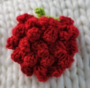 Close-up of handmade 3D crocheted strawberry charm with green leaves and red knit texture
