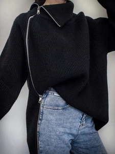 Dettaglio di un maglione nero a maglia grossa con cerniera diagonale e trama a coste verticali