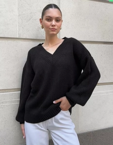 Close-up of black oversized V-neck knit sweater showing ribbed cuffs and coarse texture