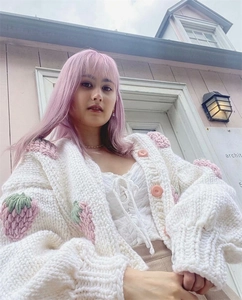 Close-up of 3D knitted strawberry details and large pink buttons on a white cardigan