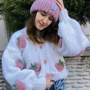 Close-up of white chunky knit cardigan featuring 3D strawberry appliques and soft wool texture