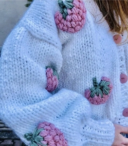 Detail of 3D strawberry hand-knitted crochet patches on white chunky knit cardigan