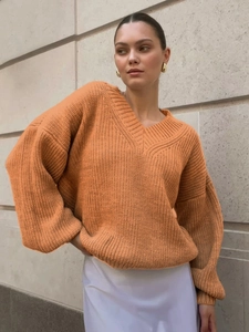 Detail view of orange oversized V-neck knit sweater with ribbed cuffs and textured fabric