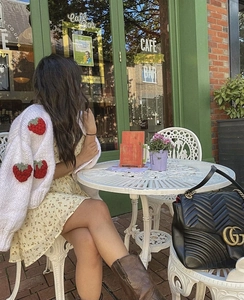 Detail of chunky knit white cardigan featuring 3D strawberry embroidery on sleeves