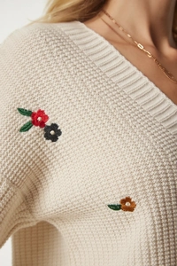 Detailaufnahme der Blumenstickerei und der groben Strickstruktur auf beige Strickjacke