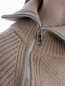 Dettaglio della trama a maglia grossa e cerniera in metallo argento su maglione beige a collo alto