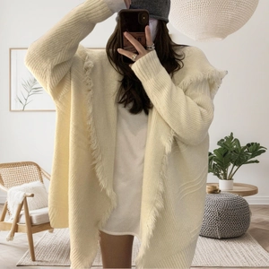 Close-up of cream knit cardigan featuring thick knit texture and decorative fringe tassels