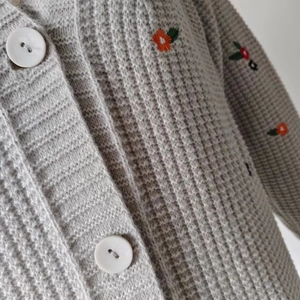 Nahaufnahme der hellgrauen Waffelstrickjacke mit Blumenstickerei und weißen Knöpfen