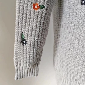Detailaufnahme der bunten Blumenstickerei auf dem grauen Grobstrick-Cardigan Ärmel