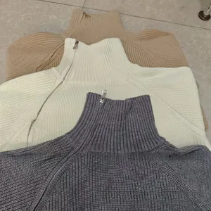 Dettaglio di tre maglioni a maglia grossa con collo a zip in beige, bianco e grigio scuro