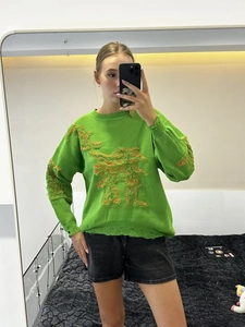 Close-up of bright green knit sweater with orange distressed ripped holes and crew neck