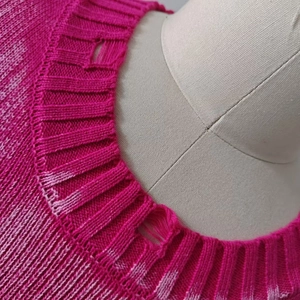 Detailed view of distressed crew neck and pink knit texture on a loose pullover sweater