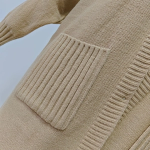 Detail of the light beige knit cardigan showing the ribbed pocket and soft fabric texture