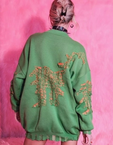 Detailed back view of green oversized knit sweater with orange shredded distress design