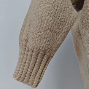 Detail of beige knit sweater showing elastic ribbed cuff and soft texture fabric