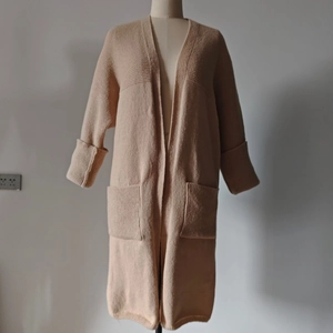 Detail of loose beige knit cardigan featuring large front pockets and long textured sleeves