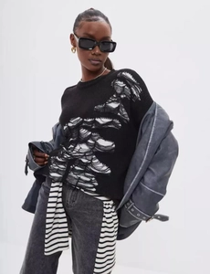 Close-up of black knitted sweater featuring distressed hollow-out and frayed thread details