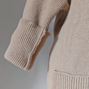 Detail view of beige knit cardigan showing ribbed cuffs and soft textured pocket fabric