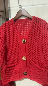 Détail d'un cardigan rouge en maille ajourée avec boutons dorés et décolleté en V