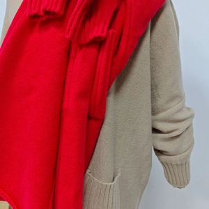 Detailed view of red knitted scarf layered over a loose beige cardigan with texture