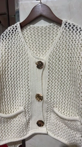 Détail de la maille ajourée sur un cardigan crème avec de grands boutons dorés