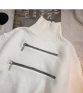 Dettaglio di un maglione bianco a collo alto con doppie cerniere in metallo e maglia