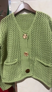 Détail d'un cardigan vert clair en maille ajourée avec boutons dorés gaufrés
