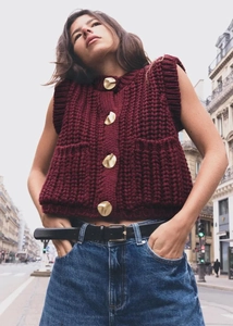 Detail of burgundy chunky knit vest featuring four decorative gold metal buttons