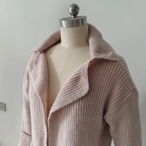 Dettaglio del cardigan in maglia rosa chiaro con polsini a coste e trama in lana spessa