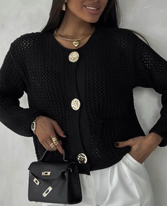 Détail d'un cardigan noir ajouré avec de gros boutons dorés en relief et poches latérales