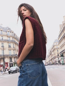 Macro texture of a burgundy chunky knit vest in a casual outdoor urban street setting