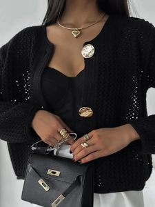 Détail du cardigan en crochet noir avec boutons dorés, collier cœur et sac à main en cuir