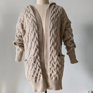 Detail of loose beige cable-knit cardigan with hood and practical side pockets
