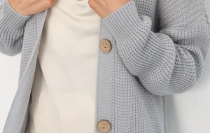 Detail of light gray chunky knit cardigan featuring large round wooden buttons and texture