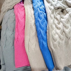 Detail showing various colors of cable knit wool sweaters with ribbed cuffs and hem