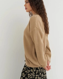 Close-up of beige round neck knit sweater featuring vertical ribbed texture and soft fabric