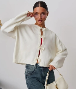 Close-up of white knitted cardigan featuring stylish front ribbon bow tie closures