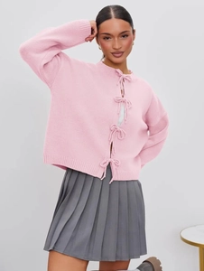 Detail of light pink knit cardigan with elegant ribbon bow ties and soft textured fabric