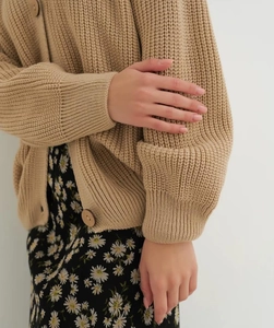 Close-up of beige waffle knit cardigan with wooden buttons and floral skirt detail