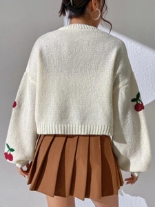 Detail of red cherry embroidery on chunky cream knit cardigan with ribbed cuffs