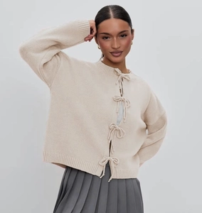 Detail of cream knit cardigan featuring elegant front bow tie closures and ribbed texture